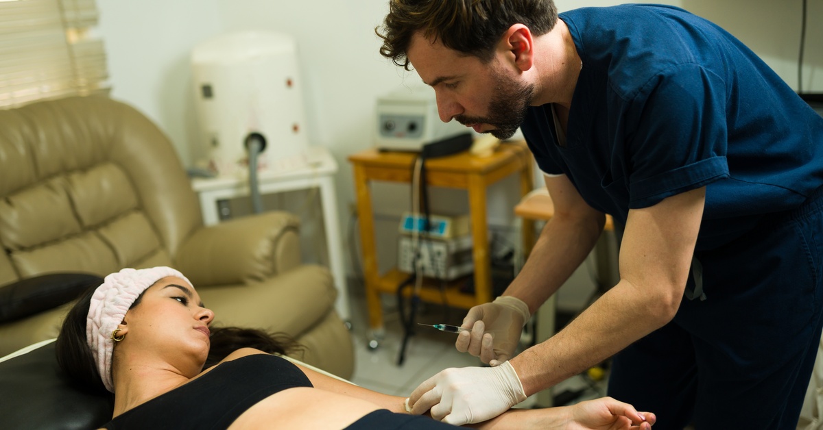A medical professional prepares to inject a patient’s arm while the patient lies on a treatment bed in a clinic.