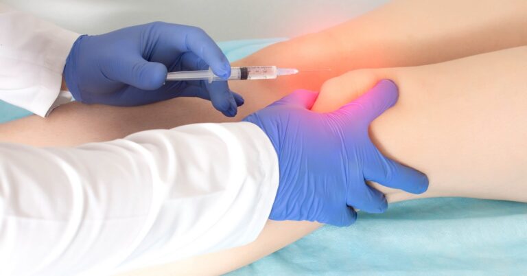 Gloved hands inject a syringe into a patient’s knee while applying pressure to the joint in a clinical setting.