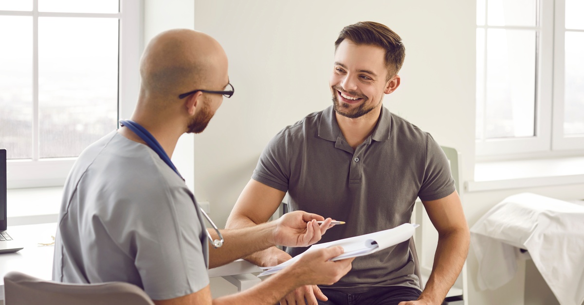 A doctor reviews paperwork with a smiling patient during a consultation in a bright medical office setting.