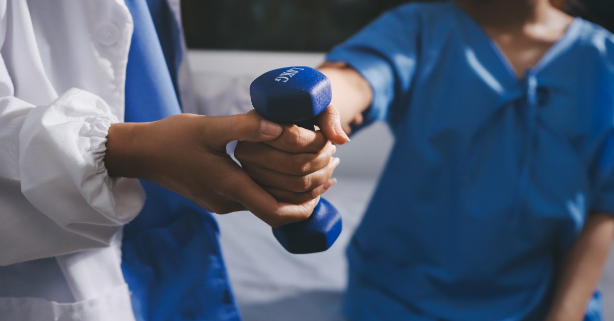 A clinician guides a patient holding a dumbbell, assisting with controlled arm movement during exercise.