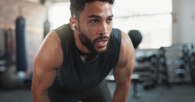 An athlete catches his breath after an intense gym workout, leaning forward as he recovers from physical exertion.