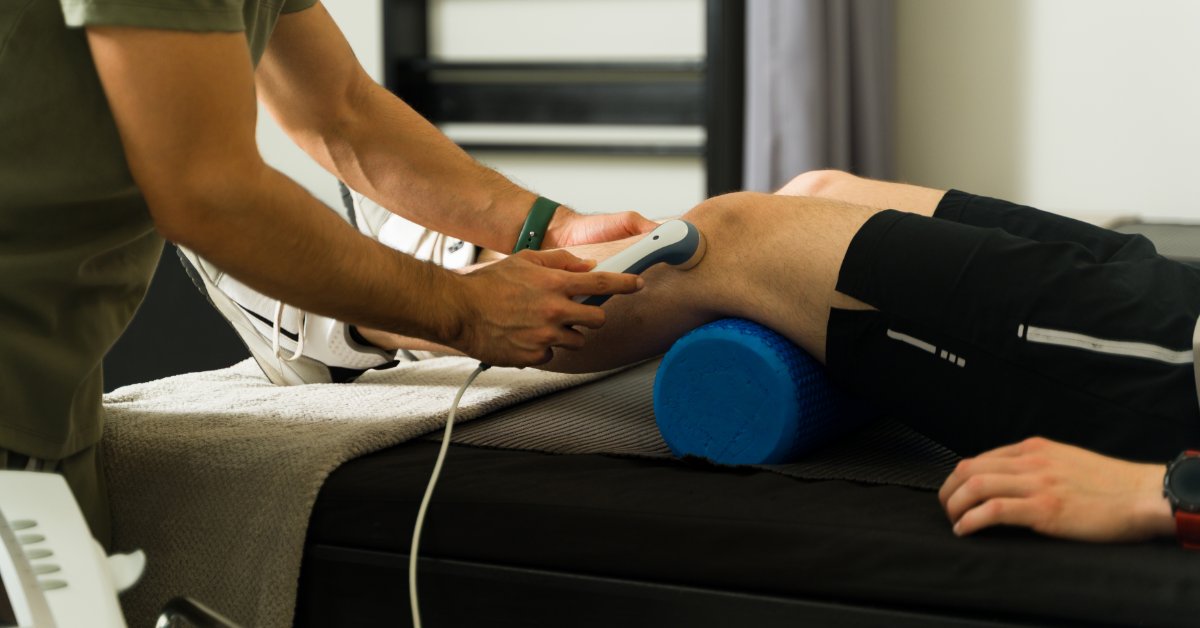 A healthcare professional holds an ultrasound machine attachment against the knee of a person lying on an exam table.