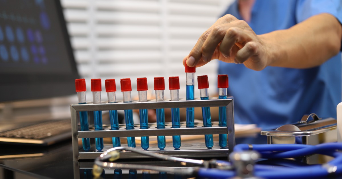 A healthcare professional handles blood samples in test tubes while working at a clinical laboratory station.