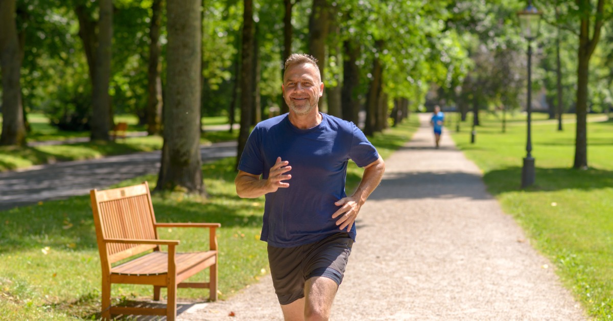 A middle-aged man runs along a tree-lined park path during an outdoor workout as part of an active lifestyle.